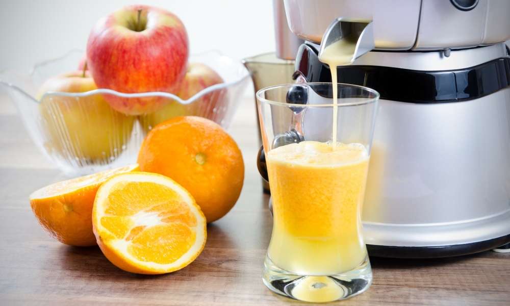 How to use a juicer with orange juice dripping from juicer into glass and cut orange and whole apples 