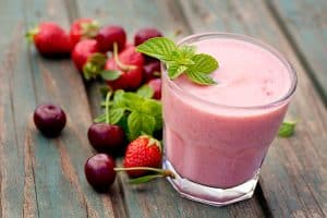 juicing at home with glass of strawberry fruit drink surrounded by fruits on wooden table