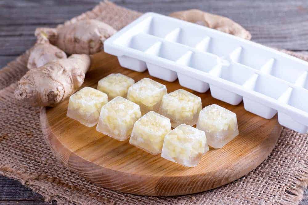 8 ice cubes of ginger juice on chopping board with empty ice cube tray and ginger roots showing how to make ginger juice frozen ice cubes 