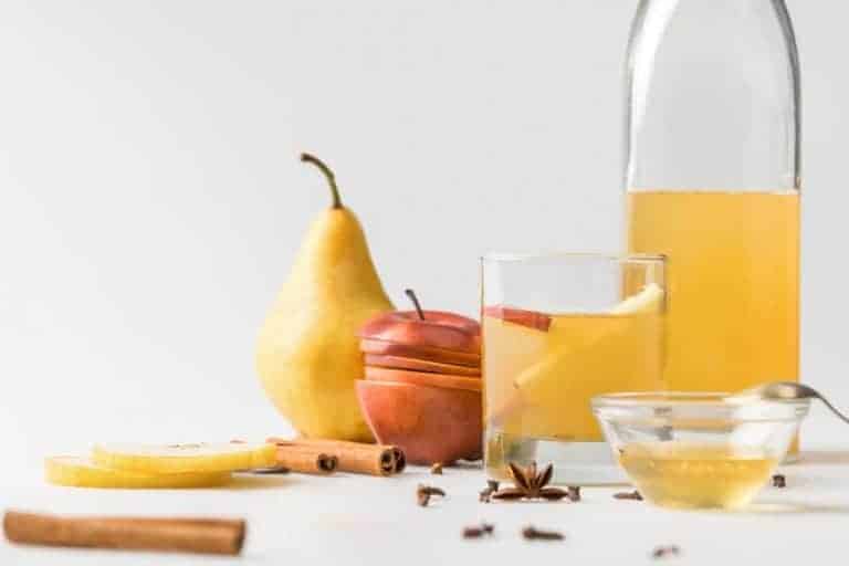 a glass of homemade juice with a half empty bottle of juice with an apple and a pear sitting beside them