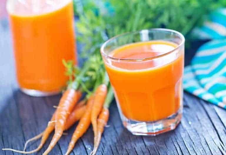 homemade juice with two glasses of carrot juice with 5 raw carrots on a wooden table