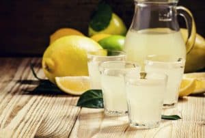 3 glasses of juice made at home and a pitcher of juice surrounded by lemons and other fruit